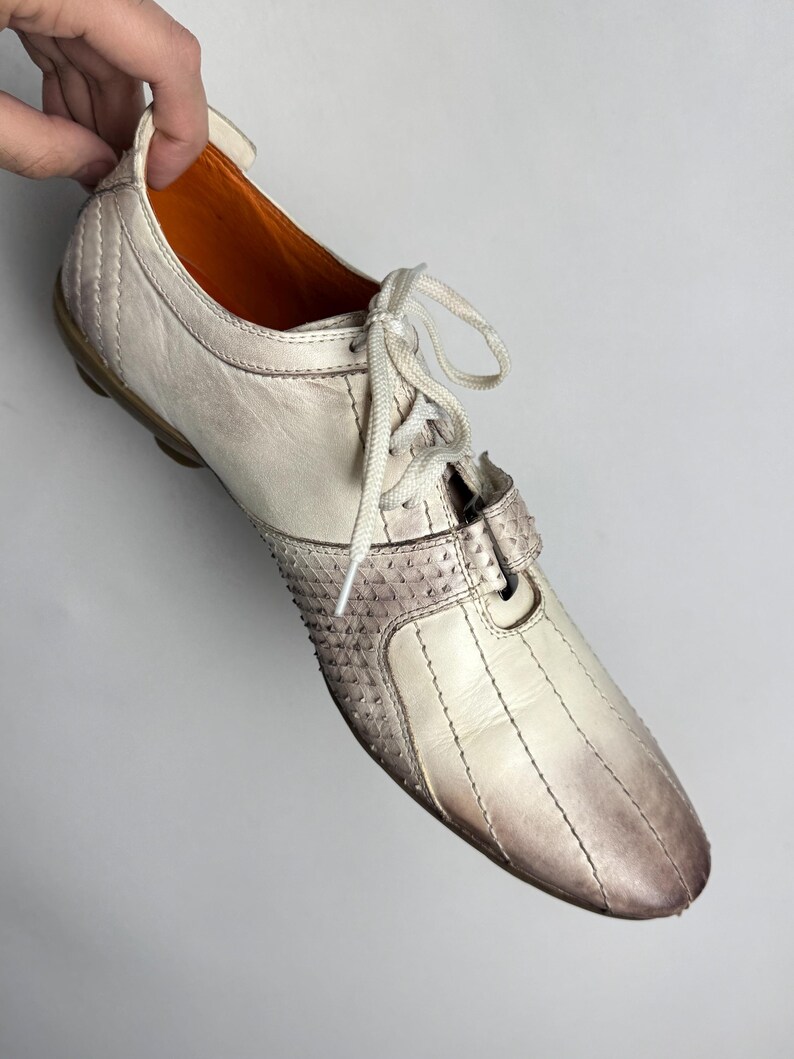 K&ouml;nnte beinhalten: Cremefarbener Ledersneaker mit strukturierter Spitze und Farbverlauf von Wei&szlig; nach Braun. Der Schuh hat wei&szlig;e Schn&uuml;rsenkel und eine braune Sohle. Der Innenraum ist orange.
