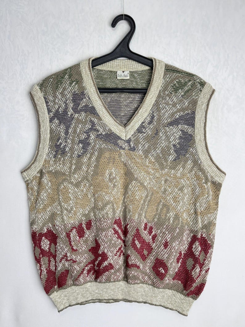May include: A vintage V-neck sweater vest with a patterned design in shades of beige, gray, green, and burgundy. The sleeveless vest is hanging on a black hanger against a white background.