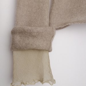 Puede incluir: Un su&eacute;ter de punto beige con un ribete de tejido beige transparente en la parte inferior de las mangas.