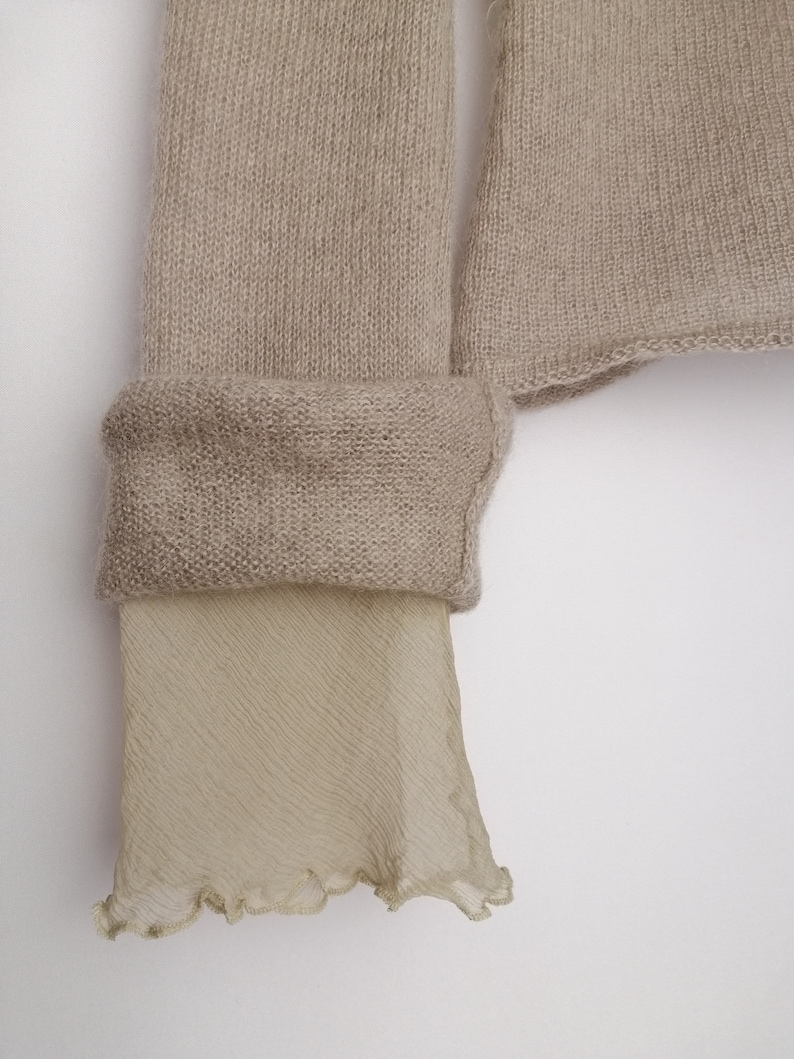 Puede incluir: Un su&eacute;ter de punto beige con un ribete de tejido beige transparente en la parte inferior de las mangas.