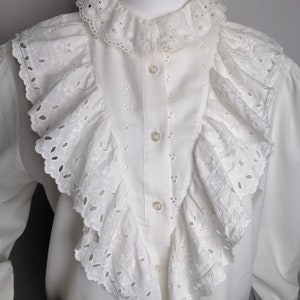 Puede incluir: Blusa blanca de algod&oacute;n con un cuello grande con volantes y detalles de ojal. El cuello est&aacute; en capas y tiene un borde festoneado.