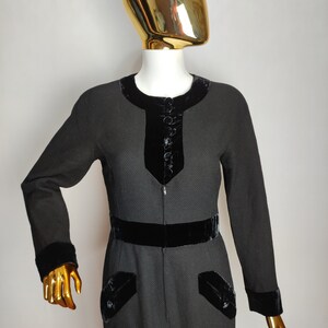 K&ouml;nnte beinhalten: Ein schwarzes Kleid mit Samtbesatz und Kn&ouml;pfen. Das Kleid hat eine figurbetonte Silhouette und einen runden Ausschnitt.