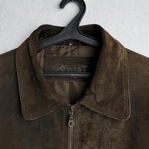 May include: A brown suede jacket with a zipper closure and a label that reads "GO WEST".