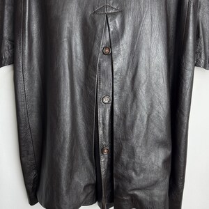 May include: A dark brown leather jacket with a button-up front. The jacket has a textured surface and a classic design. The buttons are a matching brown color. The jacket appears to be vintage or retro style.