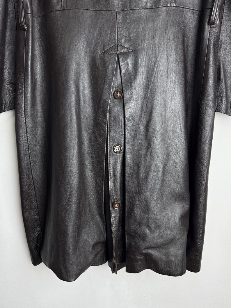 May include: A dark brown leather jacket with a button-up front. The jacket has a textured surface and a classic design. The buttons are a matching brown color. The jacket appears to be vintage or retro style.