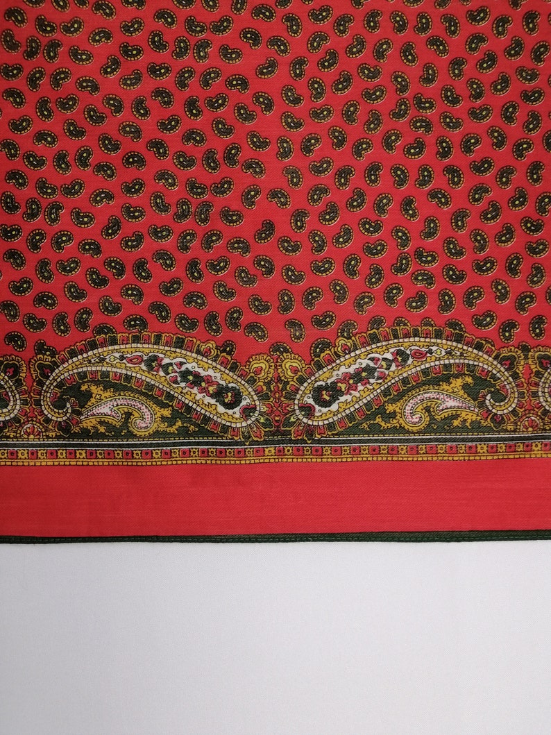 Puede incluir: Textil rojo con un estampado de cachemir de gotas negras y amarillas. El borde inferior presenta un dise&ntilde;o de cachemir m&aacute;s grande en rojo, amarillo, negro y blanco. Probablemente una bufanda o tela.