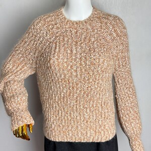 May include: A textured, light brown and white knit sweater with a crew neck and long sleeves. The sweater has a ribbed knit pattern and is displayed on a mannequin. The sleeves have a slight puff at the shoulders and taper to the wrist.