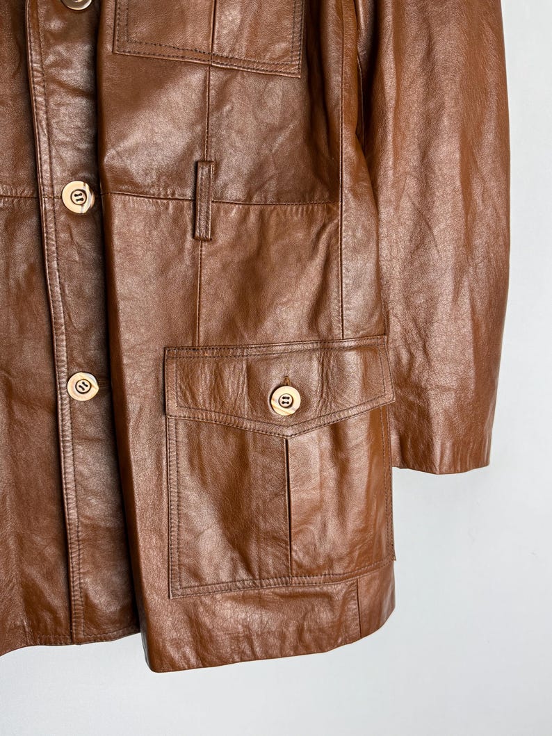 May include: A brown leather jacket with multiple pockets and gold-colored buttons. The jacket has a classic design with a button-up front and a tailored fit. The leather appears to be well-worn, giving it a vintage look.