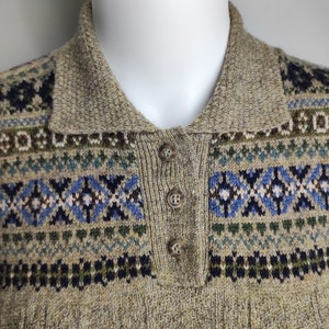 May include: A tan knit sweater with a collared neckline and three buttons. The sweater features a patterned design in blue, green, and navy. The collar and button placket are a solid tan color.
