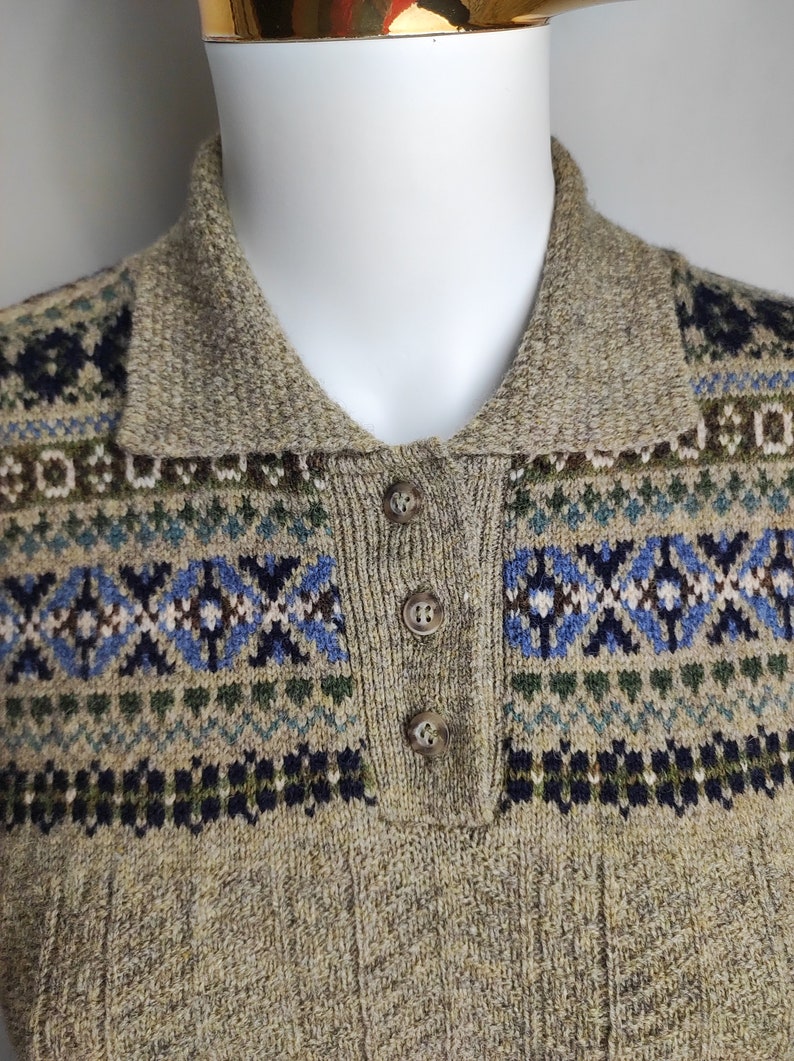 May include: A tan knit sweater with a collared neckline and three buttons. The sweater features a patterned design in blue, green, and navy. The collar and button placket are a solid tan color.