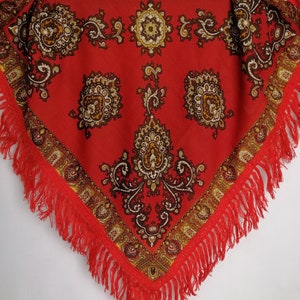K&ouml;nnte beinhalten: Ein roter Schal mit Paisley-Muster und Fransenrand. Der Schal hat ein traditionelles Design mit braunen und goldenen Akzenten.