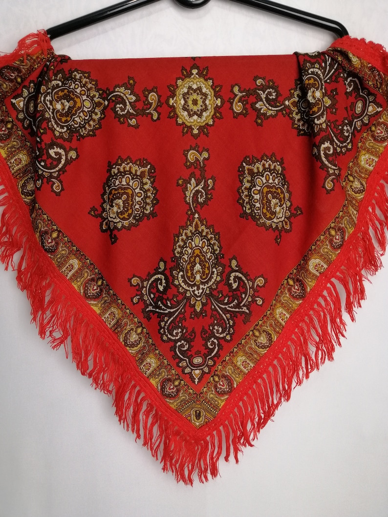 K&ouml;nnte beinhalten: Ein roter Schal mit Paisley-Muster und Fransenrand. Der Schal hat ein traditionelles Design mit braunen und goldenen Akzenten.