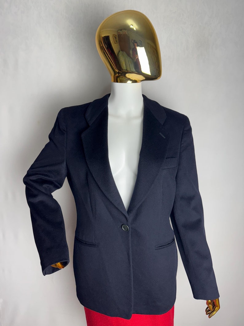 Pode incluir: Um blazer azul marinho com um &uacute;nico bot&atilde;o de fecho e mangas compridas. O blazer &eacute; feito de um tecido liso e tecido.