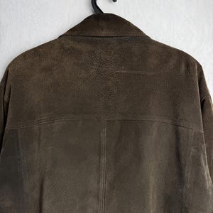 May include: A brown suede jacket with a zipper closure and a collar. The jacket is hanging on a hanger.