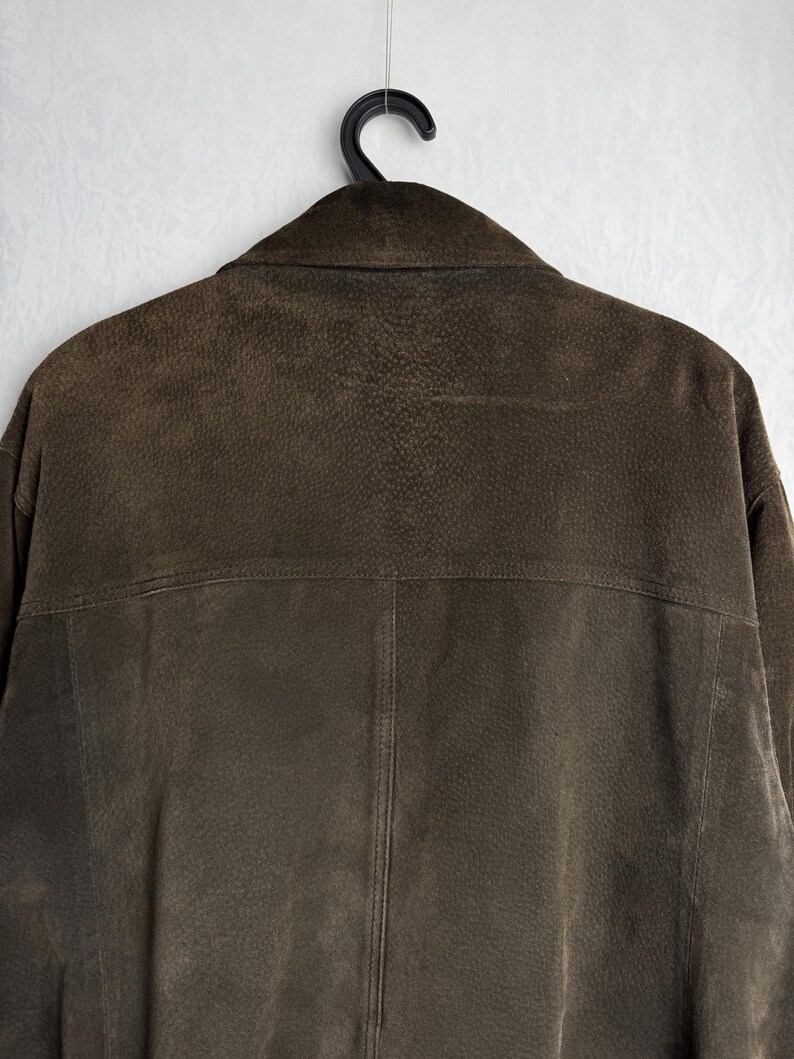 May include: A brown suede jacket with a zipper closure and a collar. The jacket is hanging on a hanger.