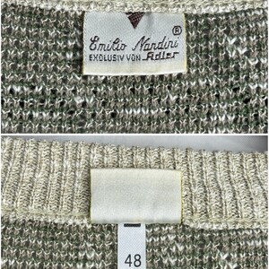 May include: Close-up of a knit sweater with a tag that reads "Emilio Nandini EXCLUSIV VON Adler". The sweater is a mix of beige, green, and white threads. The tag also has a size label with the number 48.