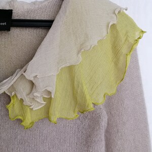 Puede incluir: Un c&aacute;rdigan de punto gris claro con un cuello de volantes hecho de una tela transparente en tonos beige y verde.