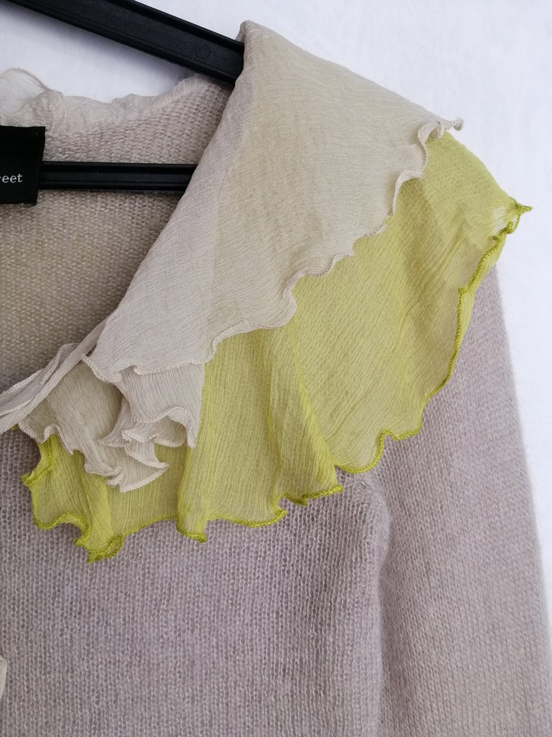 Puede incluir: Un c&aacute;rdigan de punto gris claro con un cuello de volantes hecho de una tela transparente en tonos beige y verde.