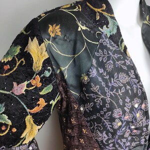 May include: A black velvet jacket with a patchwork design featuring floral patterns in shades of gold, purple, and brown. The jacket has a long sleeve and a V-neck.