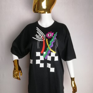 May include: Black t-shirt with a colourful abstract design featuring geometric shapes, lines, and a chequered pattern.