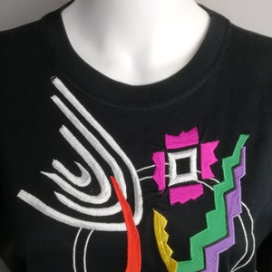 May include: Black t-shirt with a colourful abstract design featuring white, red, green, yellow, and purple embroidery.