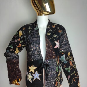 May include: A black velvet jacket with a floral embroidered design. The jacket has a tie closure and is made of a patchwork of different fabrics.