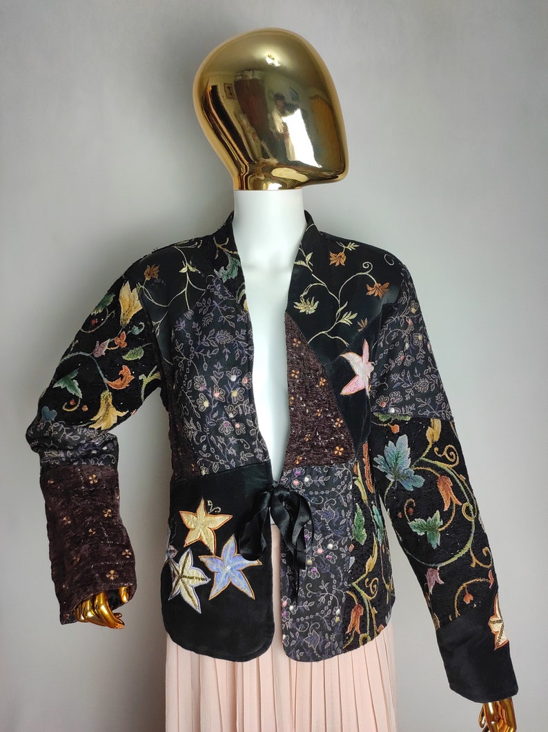 May include: A black velvet jacket with a floral embroidered design. The jacket has a tie closure and is made of a patchwork of different fabrics.
