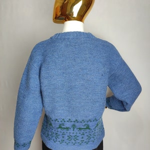 May include: A blue knitted jumper with a green and blue patterned design around the bottom hem.