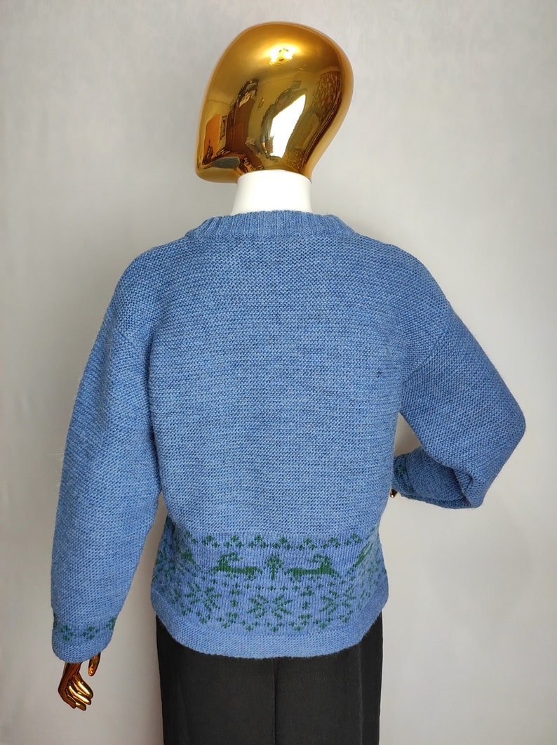 May include: A blue knitted jumper with a green and blue patterned design around the bottom hem.