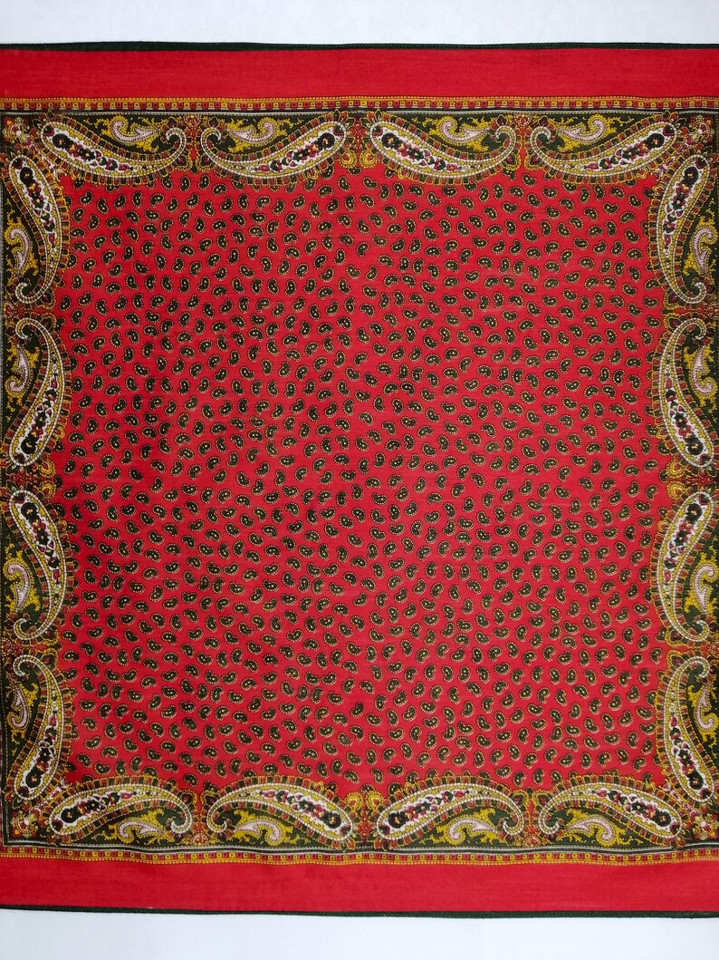 Puede incluir: Un pa&ntilde;uelo cuadrado rojo con un estampado de cachemira. El pa&ntilde;uelo tiene un patr&oacute;n repetido de peque&ntilde;as formas de cachemira negras sobre un fondo rojo. El borde presenta dise&ntilde;os de cachemira m&aacute;s grandes en amarillo, negro y blanco.