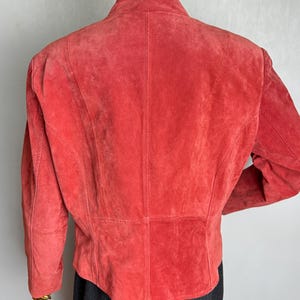 Puede incluir: Chaqueta de ante color coral con cuello alzado y mangas largas. La parte trasera de la chaqueta presenta costuras verticales y un corte entallado. La chaqueta se exhibe en un maniqu&iacute;.