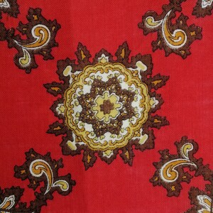 K&ouml;nnte beinhalten: Roter Stoff mit einem Paisley-Muster in Braun, Gold und Wei&szlig;. Das Muster zeigt komplizierte Wirbel und florale Motive.