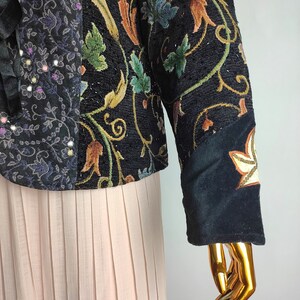 May include: A black velvet jacket with a patchwork design featuring floral embroidery and sequins. The jacket has long sleeves and a fitted silhouette.