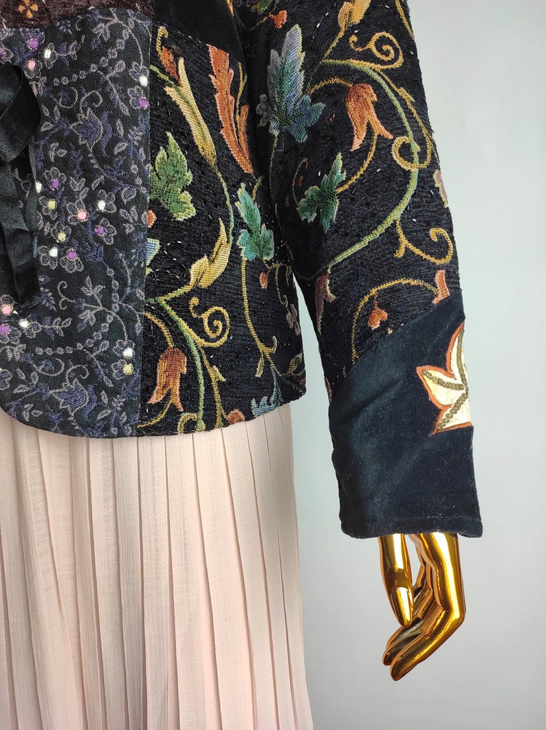 May include: A black velvet jacket with a patchwork design featuring floral embroidery and sequins. The jacket has long sleeves and a fitted silhouette.