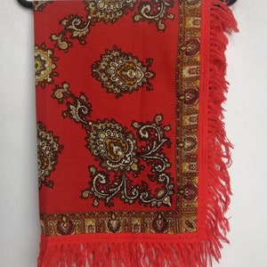 K&ouml;nnte beinhalten: Ein roter Schal mit Paisley-Muster und Fransenrand. Der Schal h&auml;ngt an einem schwarzen Kleiderb&uuml;gel.