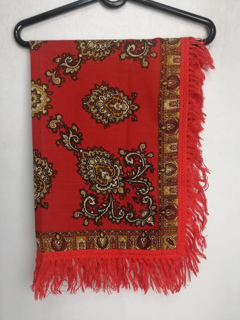 K&ouml;nnte beinhalten: Ein roter Schal mit Paisley-Muster und Fransenrand. Der Schal h&auml;ngt an einem schwarzen Kleiderb&uuml;gel.