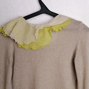 Puede incluir: Un su&eacute;ter de punto beige con un cuello de volantes en tonos amarillos y blancos.