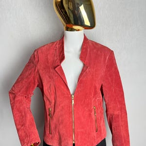 Puede incluir: Chaqueta de ante color coral con cuello alzado y cremallera completa. La chaqueta tiene dos bolsillos con cremallera y mangas largas. La chaqueta se exhibe en un maniqu&iacute;.