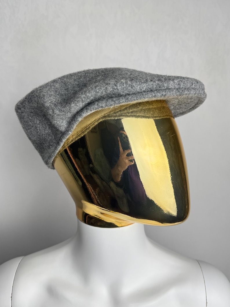 Pode incluir: Bon&eacute; plano cinzento de l&atilde;, com coroa arredondada e aba curta e r&iacute;gida. O chap&eacute;u &eacute; exibido em uma cabe&ccedil;a de manequim dourada sobre um fundo branco. O bon&eacute; &eacute; um estilo cl&aacute;ssico, adequado para v&aacute;rias ocasi&otilde;es.