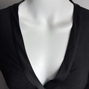 K&ouml;nnte beinhalten: Ein schwarzer Strickcardigan mit tiefem V-Ausschnitt und Satinbesatz. Der Cardigan hat einen Knopfverschluss und eine Schleife an der Taille.