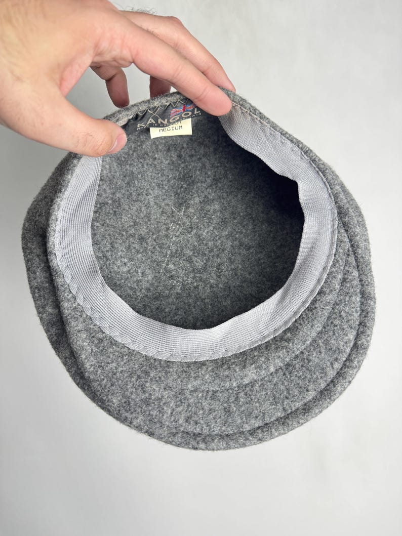 Pode incluir: Um bon&eacute; Kangol de l&atilde; cinza, visto por dentro. O bon&eacute; tem uma coroa estruturada e arredondada e uma aba r&iacute;gida. O interior apresenta uma faixa branca e uma etiqueta com o logotipo Kangol e a palavra "MEDIUM".