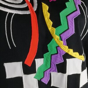 May include: Black fabric with colourful embroidered geometric shapes. The shapes include a spiral, a zig-zag, a curved line, and a chequered pattern.
