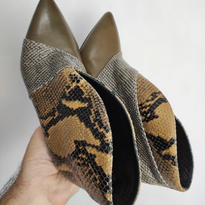 May include: A pair of brown and black snakeskin ankle boots with a pointed toe. The boots have a green leather panel at the top.
