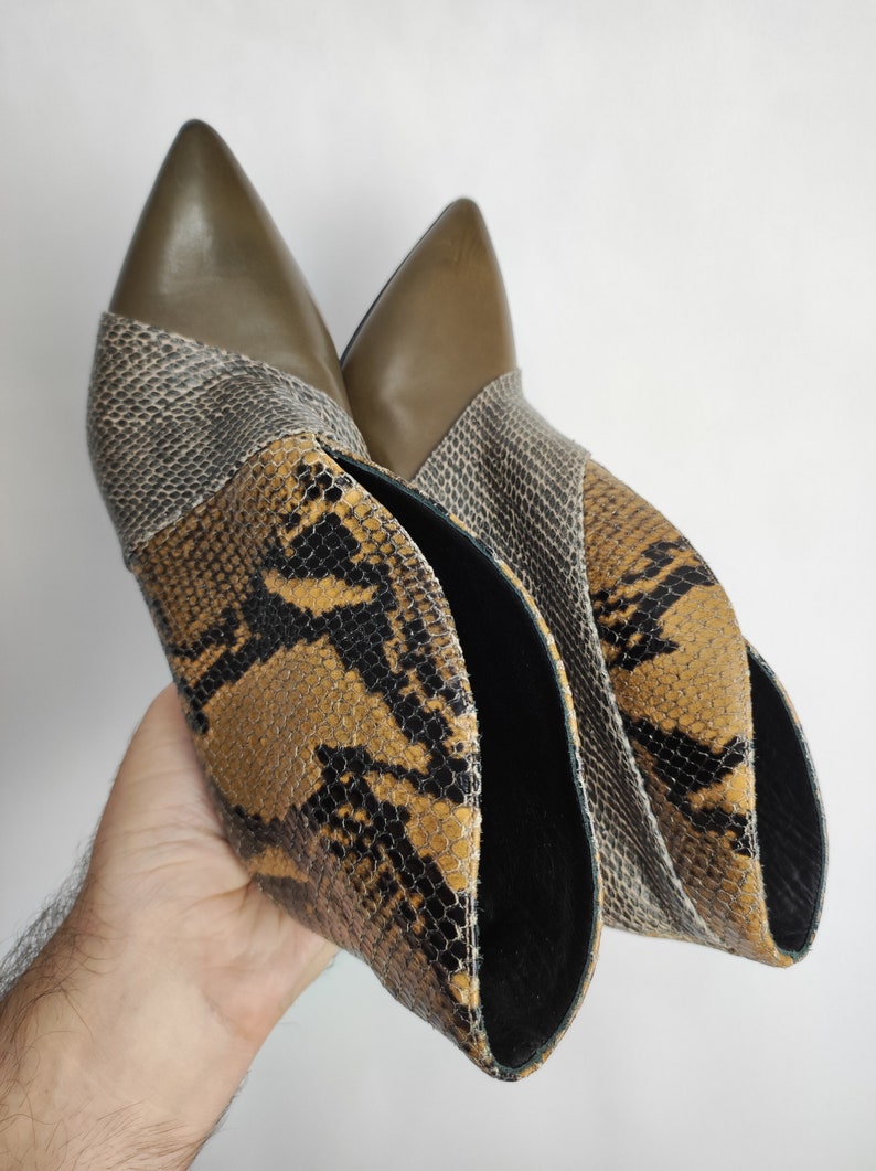 May include: A pair of brown and black snakeskin ankle boots with a pointed toe. The boots have a green leather panel at the top.