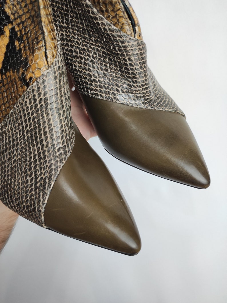 May include: A pair of brown leather ankle boots with a snakeskin pattern on the upper part of the boot. The boots have a pointed toe and a low heel.