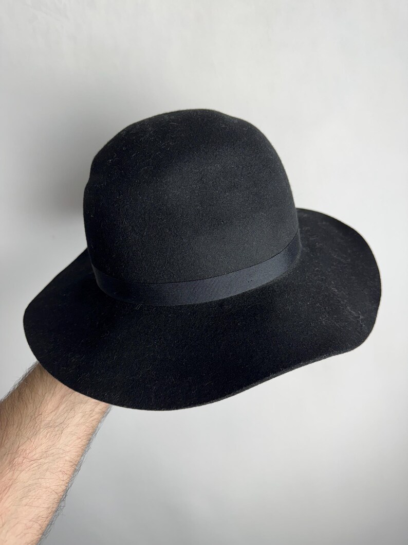 Puede incluir: Un sombrero fedora de fieltro negro con ala ancha y una cinta negra.