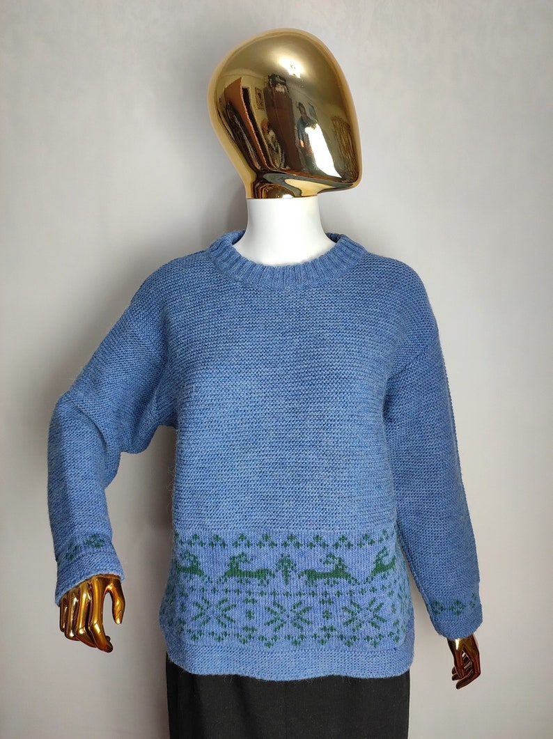 May include: A blue knitted jumper with a green reindeer pattern around the bottom hem.