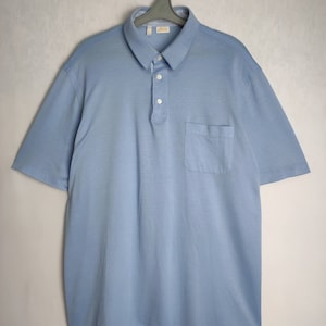 May include: A light blue short-sleeved polo shirt with a single button placket and a chest pocket.