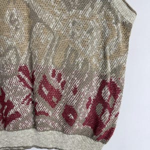 May include: A sleeveless sweater with a patterned design in shades of beige, gray, and burgundy. The sweater has a ribbed hem and neckline. The knitwear has a mesh-like texture.