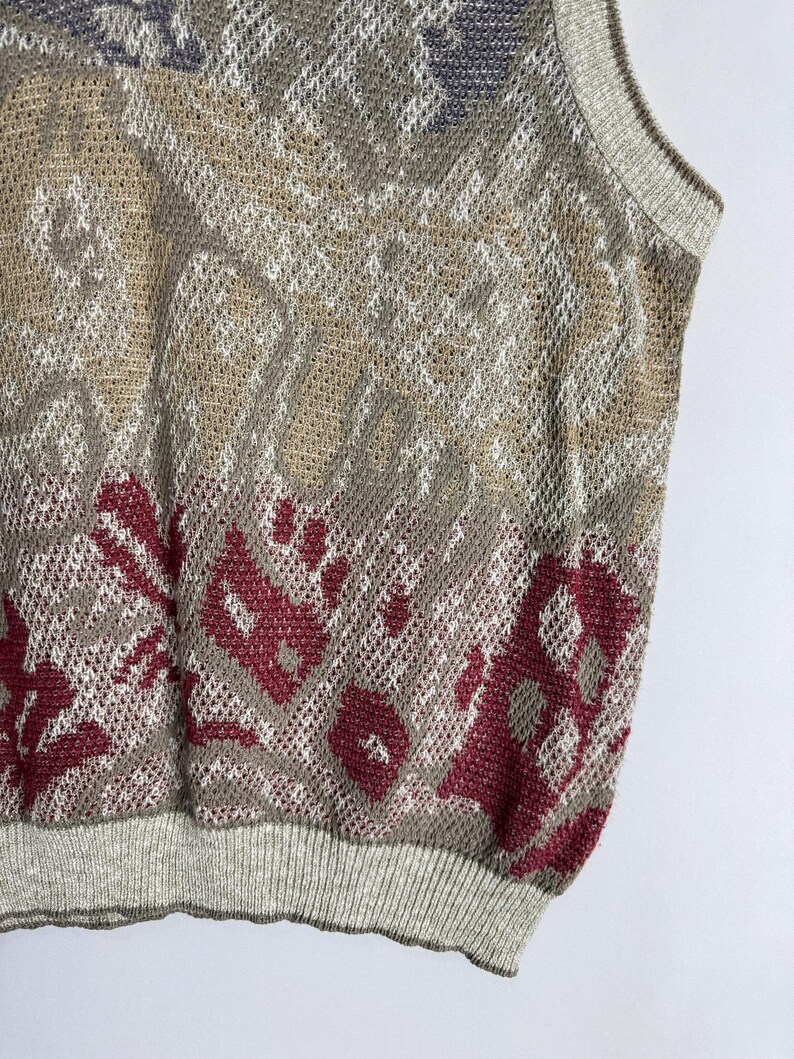 May include: A sleeveless sweater with a patterned design in shades of beige, gray, and burgundy. The sweater has a ribbed hem and neckline. The knitwear has a mesh-like texture.